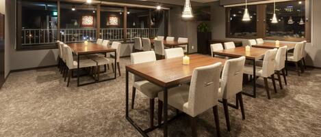 A conference room with multiple tables and chairs, large windows with city views, and pendant lighting.