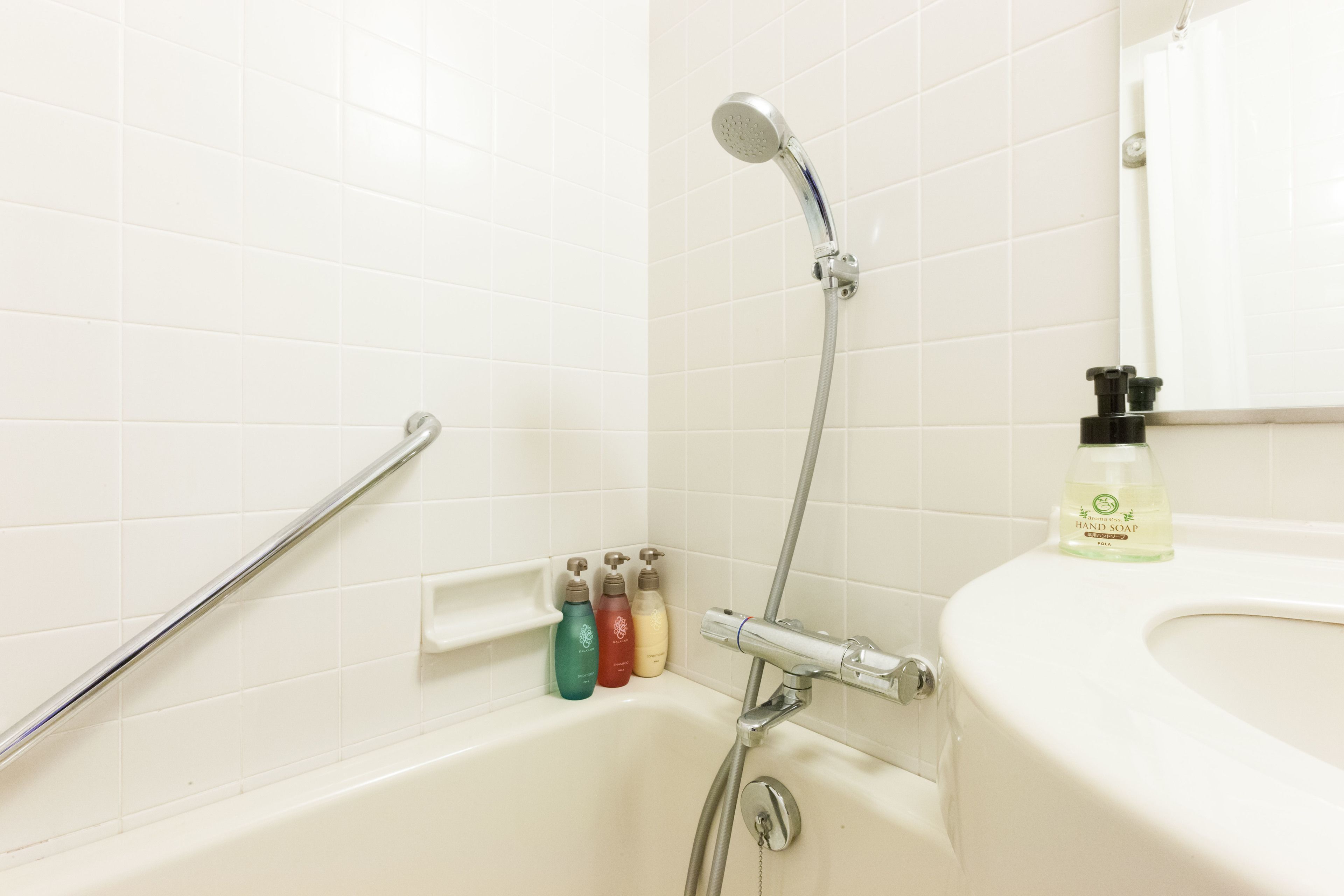 A bathroom with a bathtub, a shower, and a sink. There are hand soap bottles on the sink.