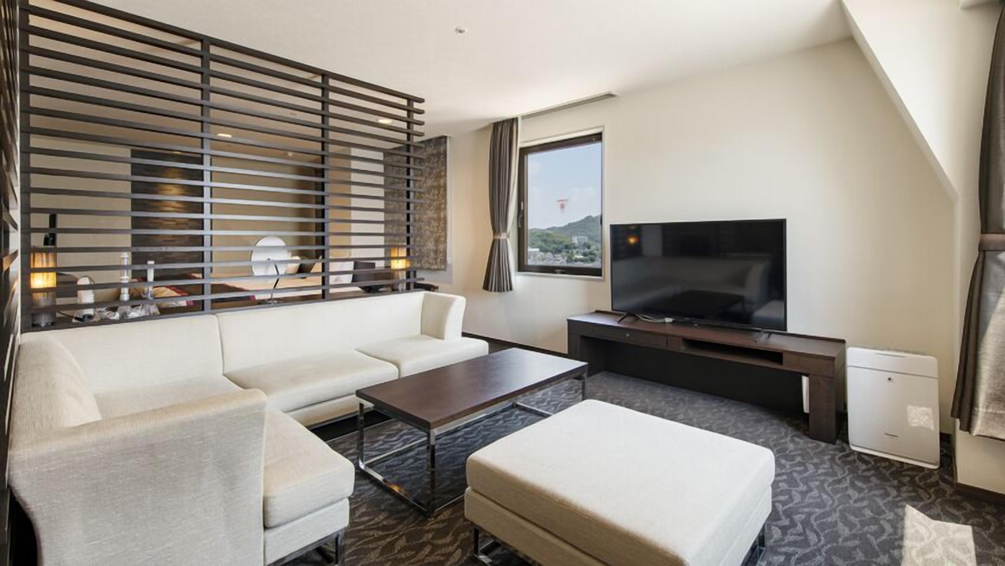 Habitación de hotel con sofá, mesa de centro, televisión y ventana con vistas.