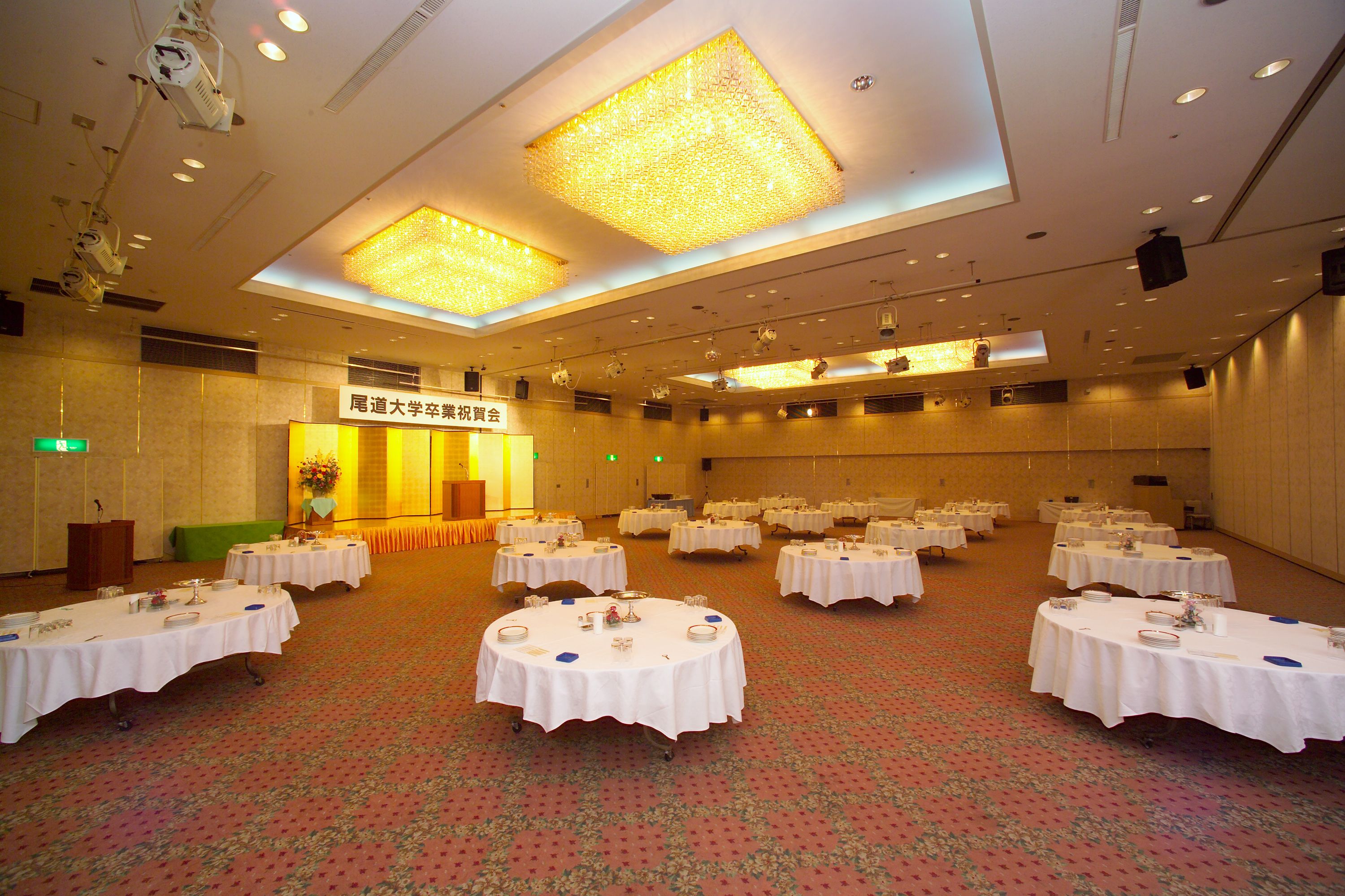 Un salón de conferencias con varias mesas redondas, cada una con mantel blanco y centros de mesa.