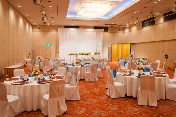 A banquet hall with round tables, white tablecloths, and chairs with white covers. - Onomichi Kokusai Hotel (Onomichi)