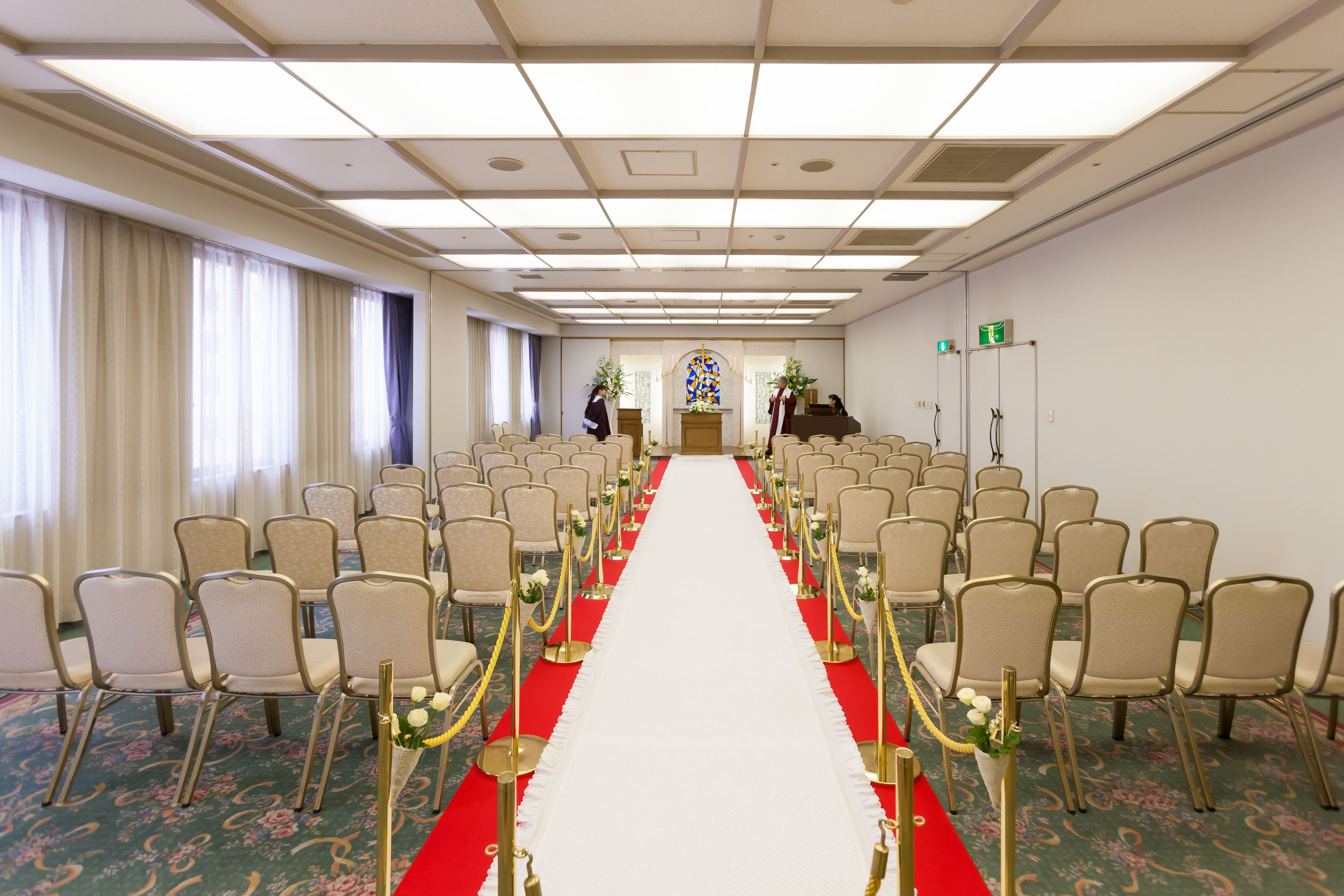 A conference room with rows of chairs, a red carpet, and a floral carpet design.
