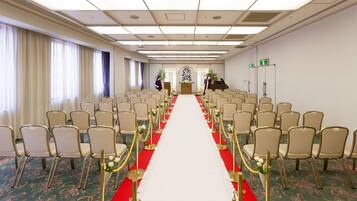 A conference room with rows of chairs, a red carpet, and a floral carpet design.