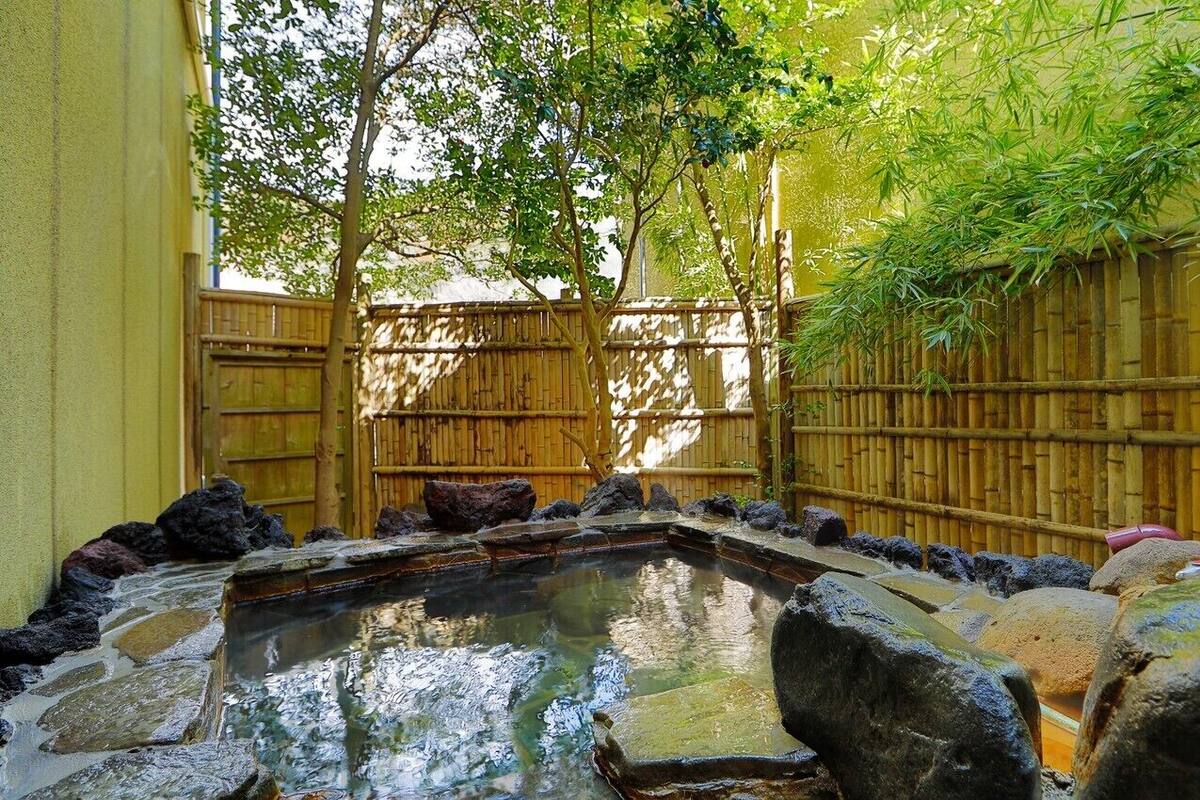 A traditional Japanese garden with a stone pond, bamboo fence, and large rocks.