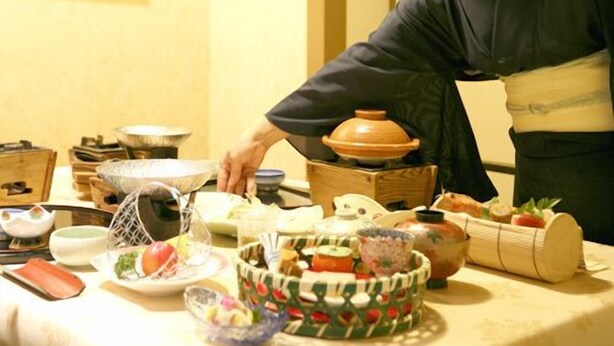 Una persona in abiti tradizionali che serve cibo a un tavolo imbandito con diversi piatti e utensili.
