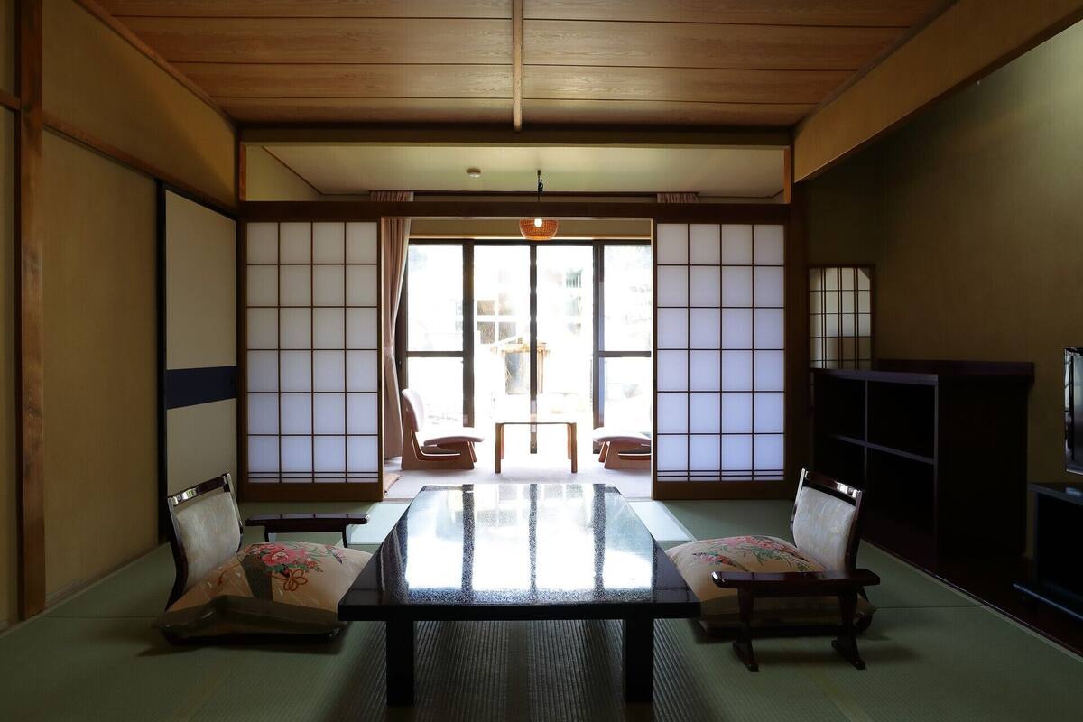 A traditional Japanese room with tatami flooring, a low table, two chairs, a television, and sliding shoji screens.