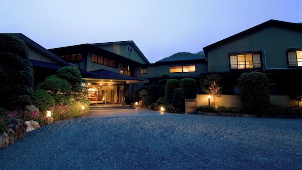 A multi-story building with a well-lit entrance, surrounded by landscaped gardens and a gravel driveway. - Hotel Kawachiya Izu Shimogamo Onsen (Minamiizu)