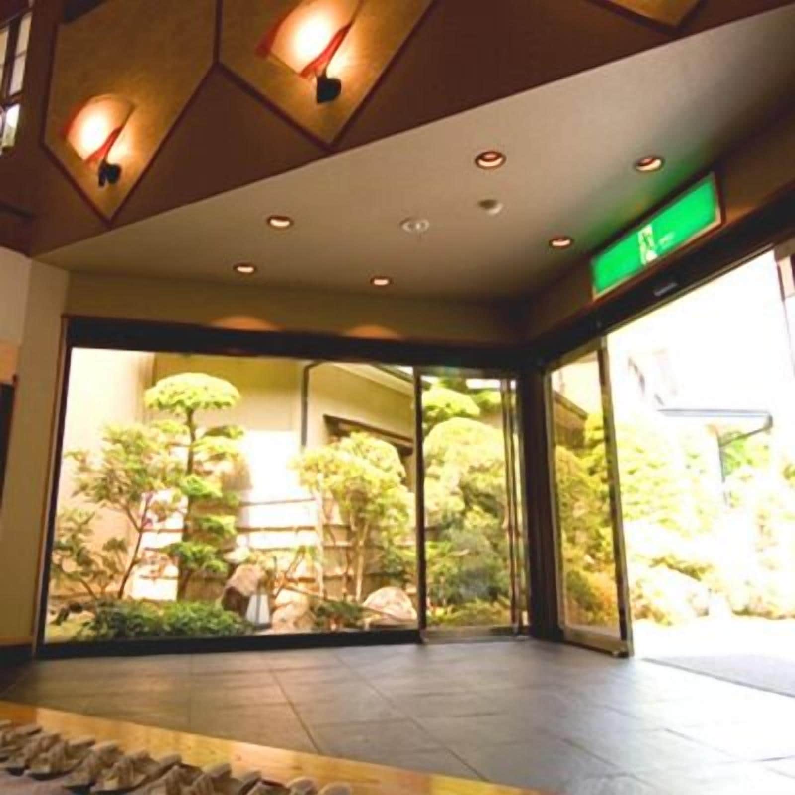 Um hall de hotel com entrada de vidro, piso de pedra e vista para um jardim com árvores e pedras.