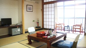 Une pièce de style japonais traditionnel, avec un sol recouvert de tatamis, une petite table basse avec un service à thé, un téléviseur et une porte coulissante donnant sur un balcon.