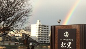 Un bâtiment avec une enseigne devant, un arbre et un arc-en-ciel en arrière-plan.