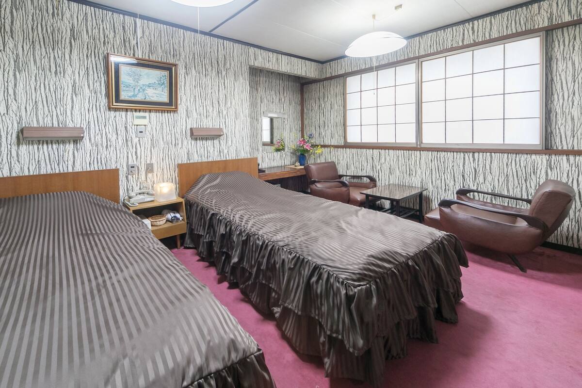 A hotel room with two beds, a desk, a chair, and a large window.