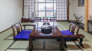 Une pièce de style japonais traditionnel, avec un sol recouvert de tatamis, une table basse au plateau laqué noir et des chaises en bois avec des coussins.