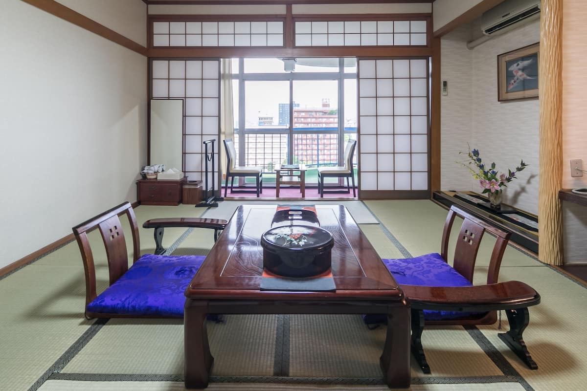 A traditional Japanese room with tatami flooring, a low table with a black lacquered top, and wooden chairs with cushions.