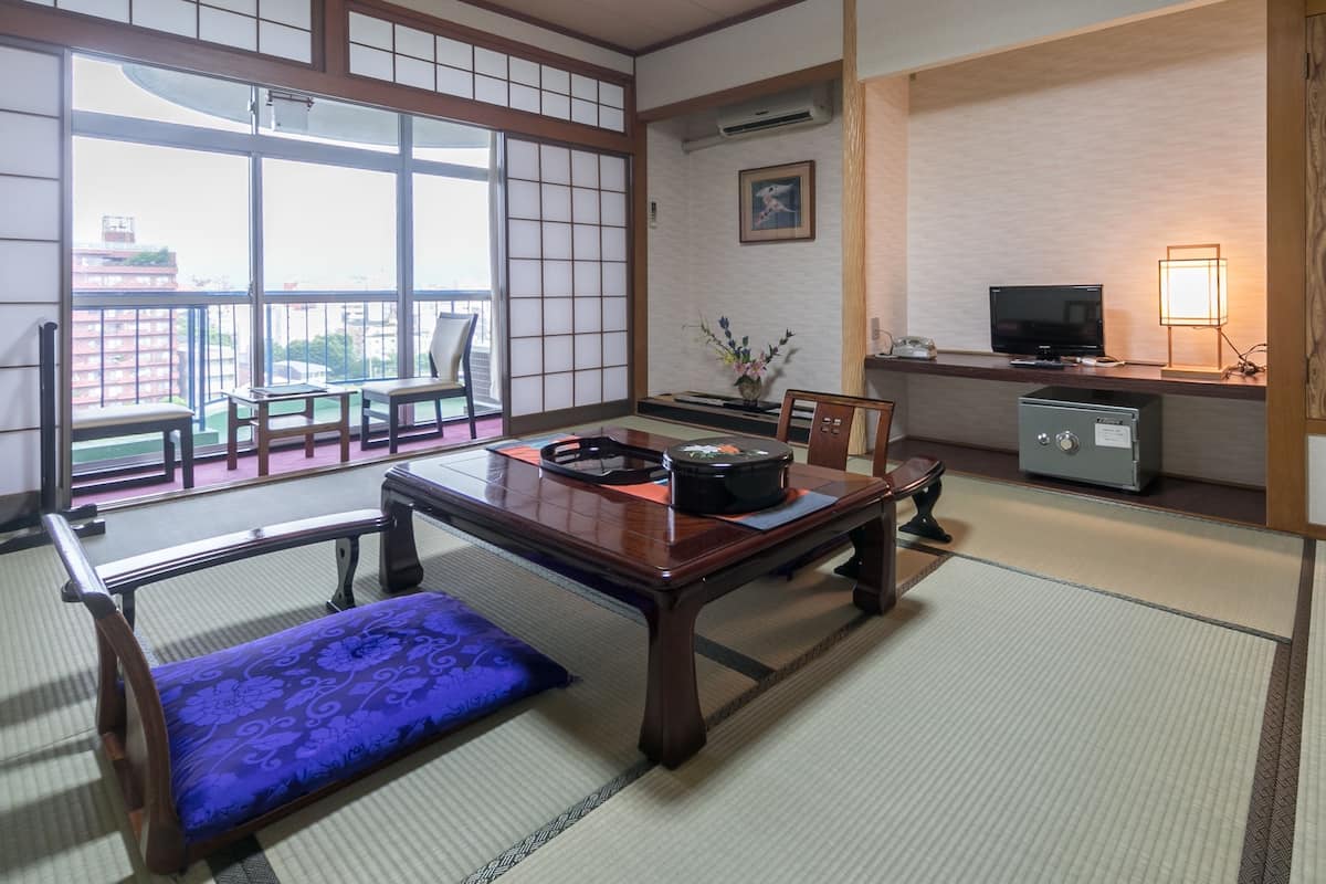 A traditional Japanese room with tatami flooring, a low table with a cushion, a television, and a cabinet.