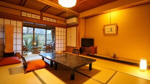 A traditional Japanese room with tatami flooring, a low table, chairs, a television, and a sliding door leading to a garden. - Saneatsu No Yado Izumiso (Shizuoka)