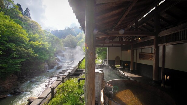 A traditional Japanese onsen with a wooden bathhouse, a hot spring, and a view of a forested valley. - Hotel Sansuiso Tsuchiyu Spa Fukushima (Fukushima)