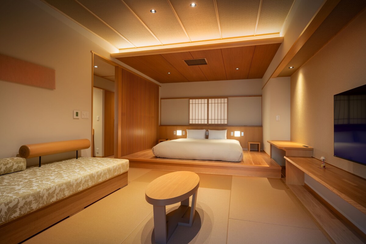 Una habitación de hotel moderna con una cama grande, un sofá, una mesita y un televisor.