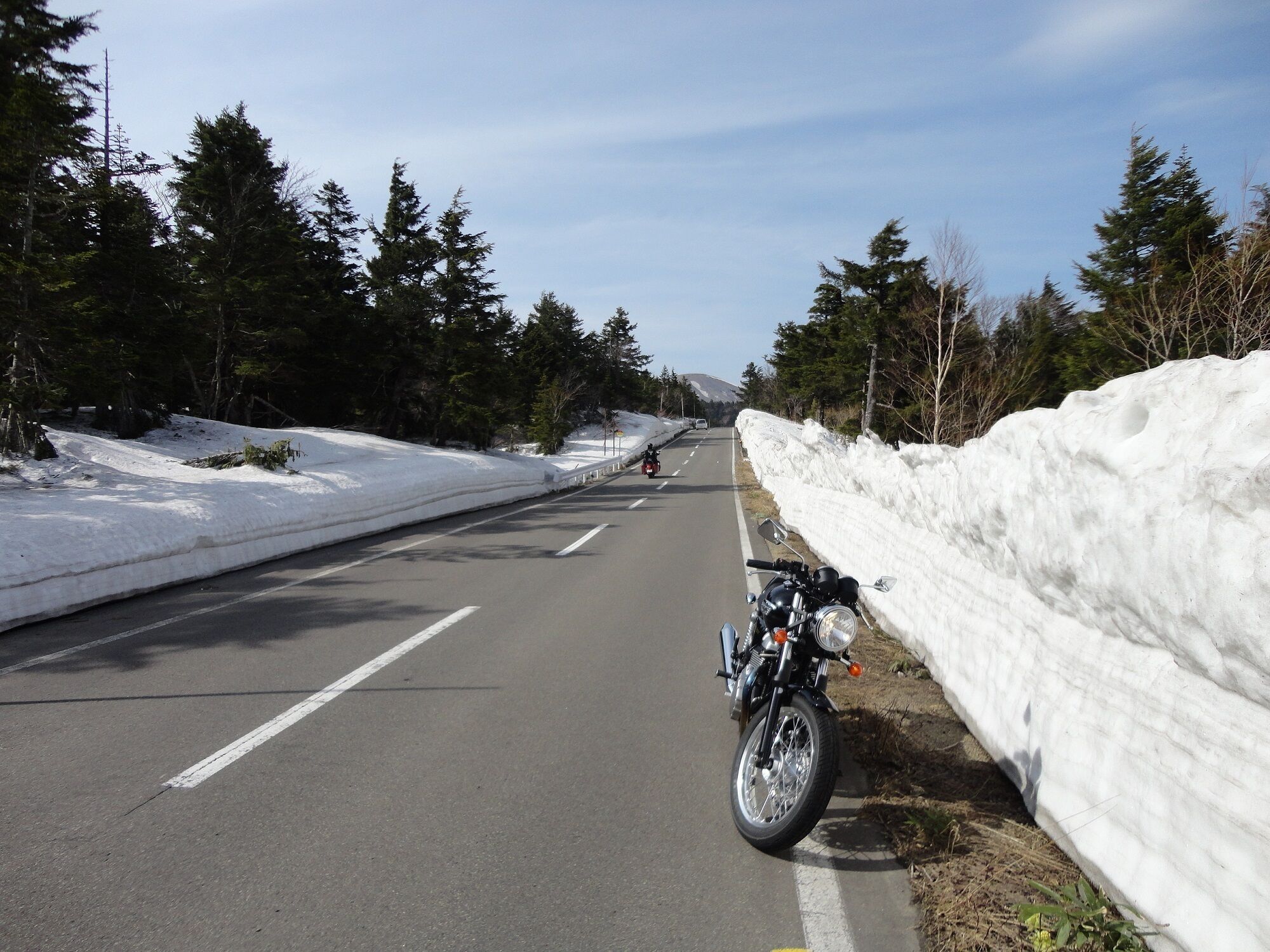 Een weg met sneeuw langs de randen, een motorfiets geparkeerd aan de rechterkant.