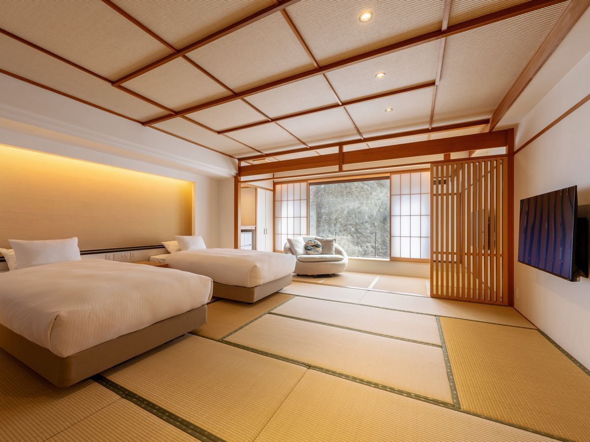 A traditional Japanese-style room with tatami flooring, a bed, a sofa, and a sliding door leading to a balcony.