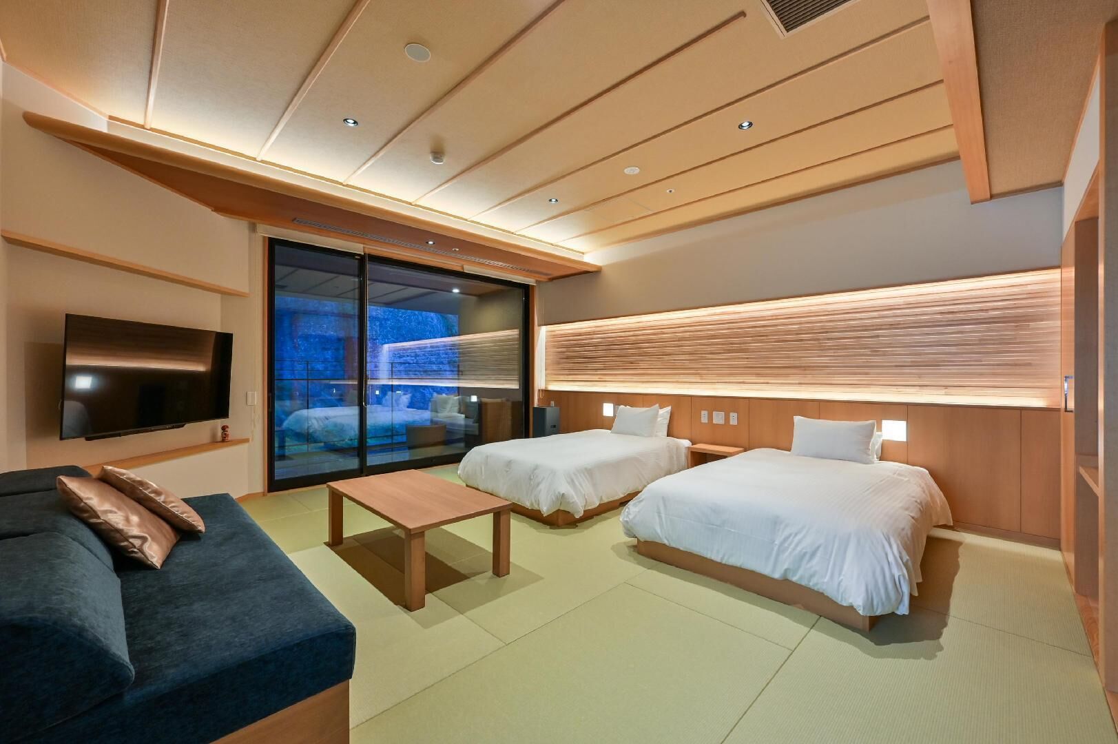 A modern hotel room with a flat-screen TV, two beds, a sofa, a sliding glass door, and a wooden ceiling.