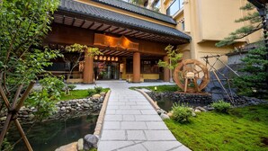 A traditional Japanese building with a stone pathway leading to a pond, surrounded by greenery and a large wooden water wheel. - Hotel Sansuiso Tsuchiyu Spa Fukushima (Fukushima)