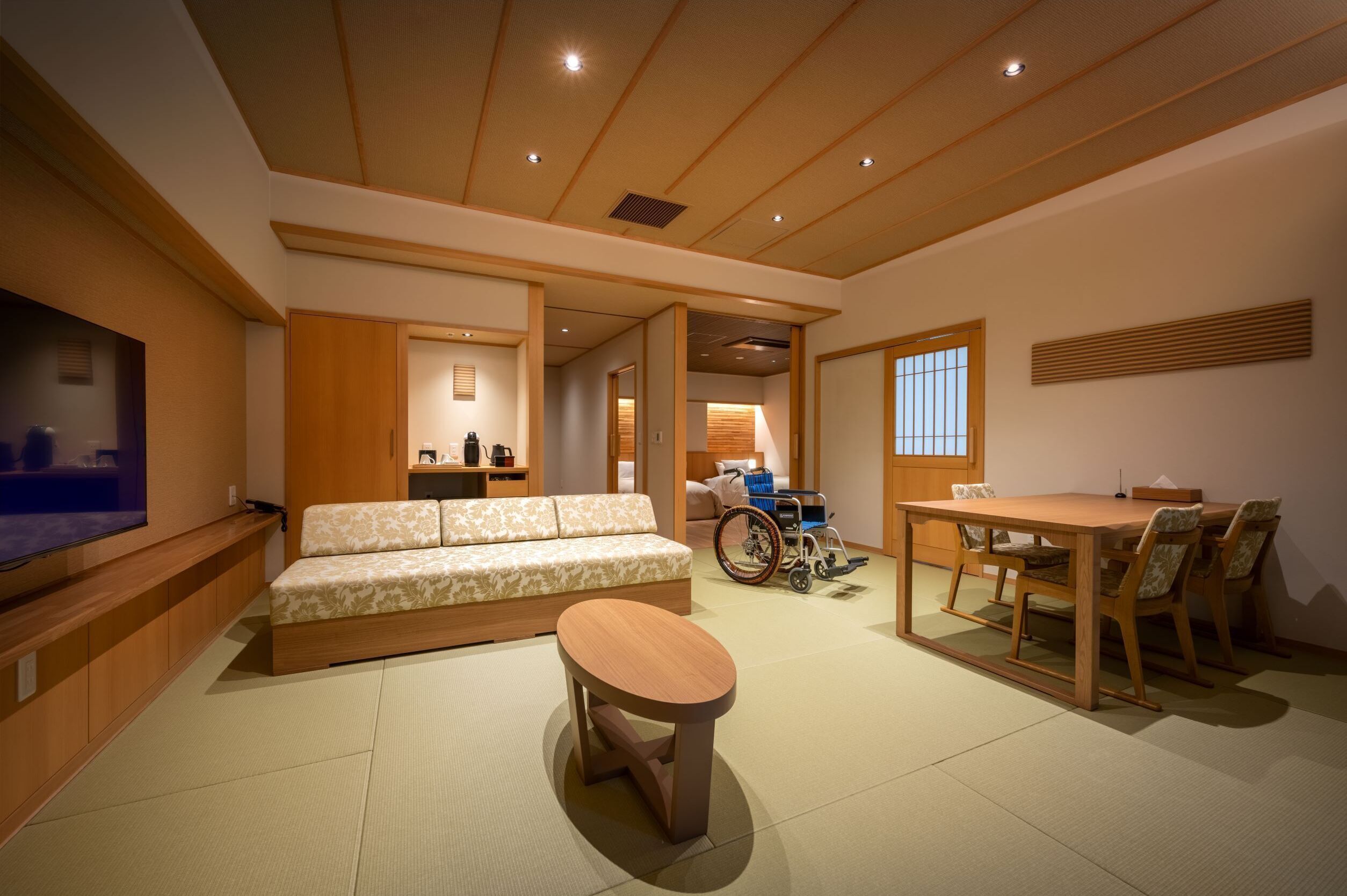 A traditional Japanese-style room with tatami flooring, a low wooden table, a sofa, and a wheelchair.