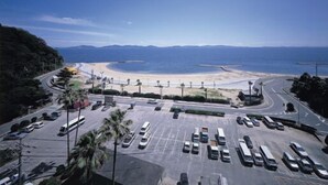 A parking lot with vehicles, a beach, and a mountainous backdrop. - Nishiura Grand Hotel Kikkei (Gamagori)