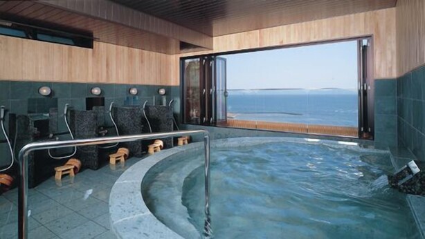 A modern indoor swimming pool with a curved edge, wooden steps, and a view of the sea through large windows. - Nishiura Grand Hotel Kikkei (Gamagori)