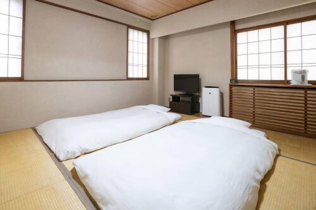 Ein Zimmer mit zwei Betten, einem Fernseher und einer kleinen Küchenzeile.