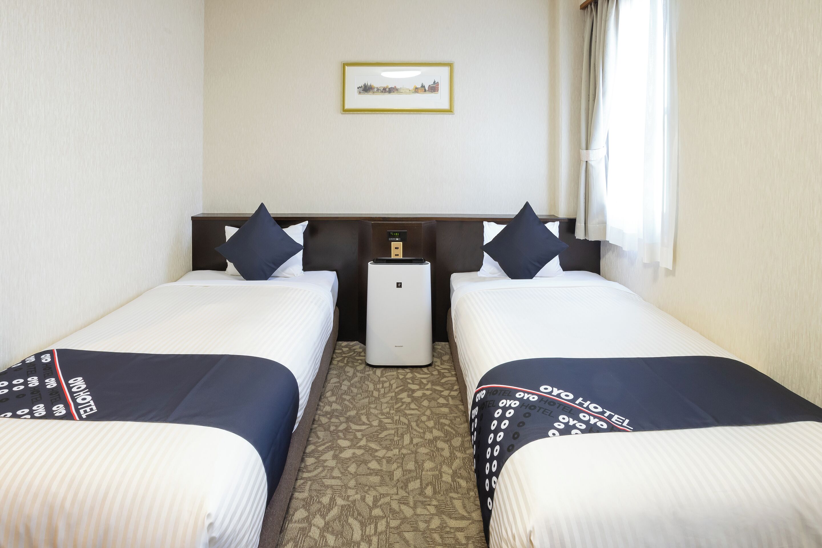 A hotel room with two beds, a nightstand, a small table, and a wall-mounted clock.