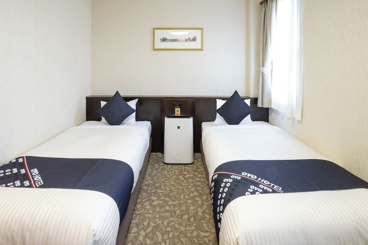 Ein Hotelzimmer mit zwei Betten, einem Nachttisch, einem kleinen Tisch und einer an der Wand befestigten Uhr.