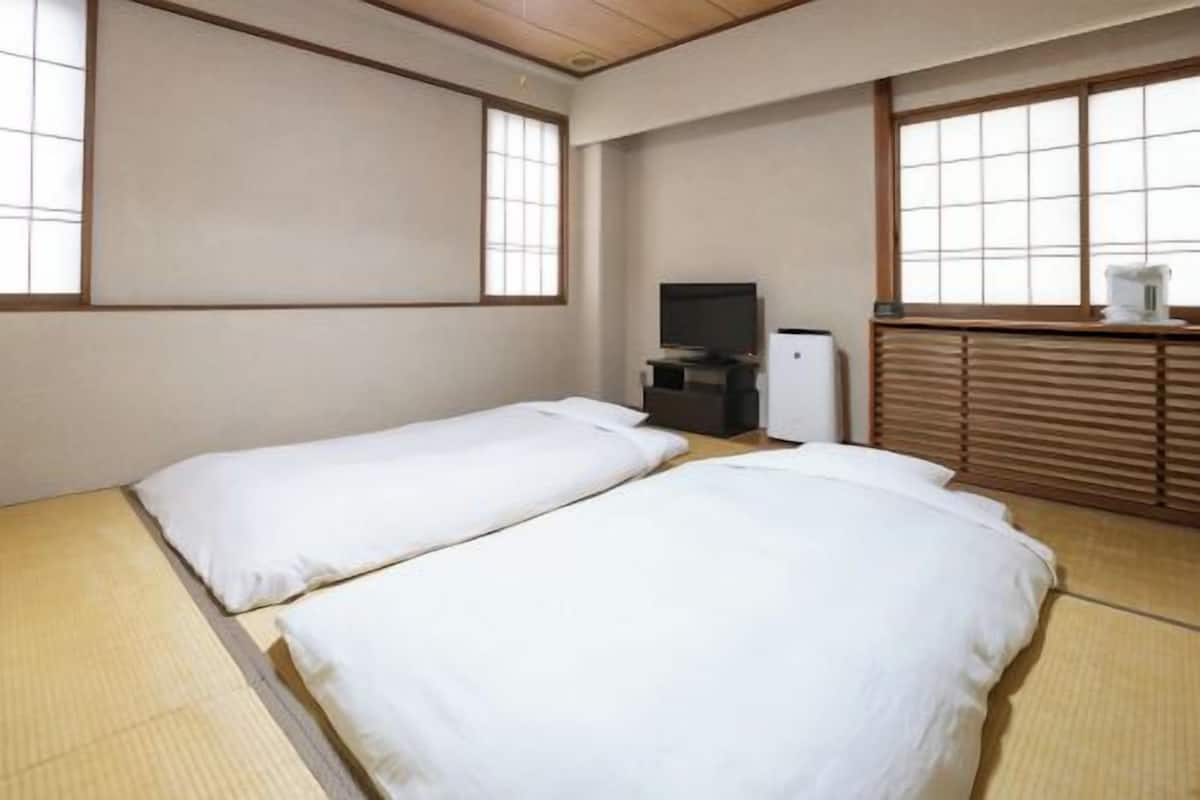 Ein Zimmer mit zwei Betten, einem Fernseher und einer kleinen Küchenzeile.