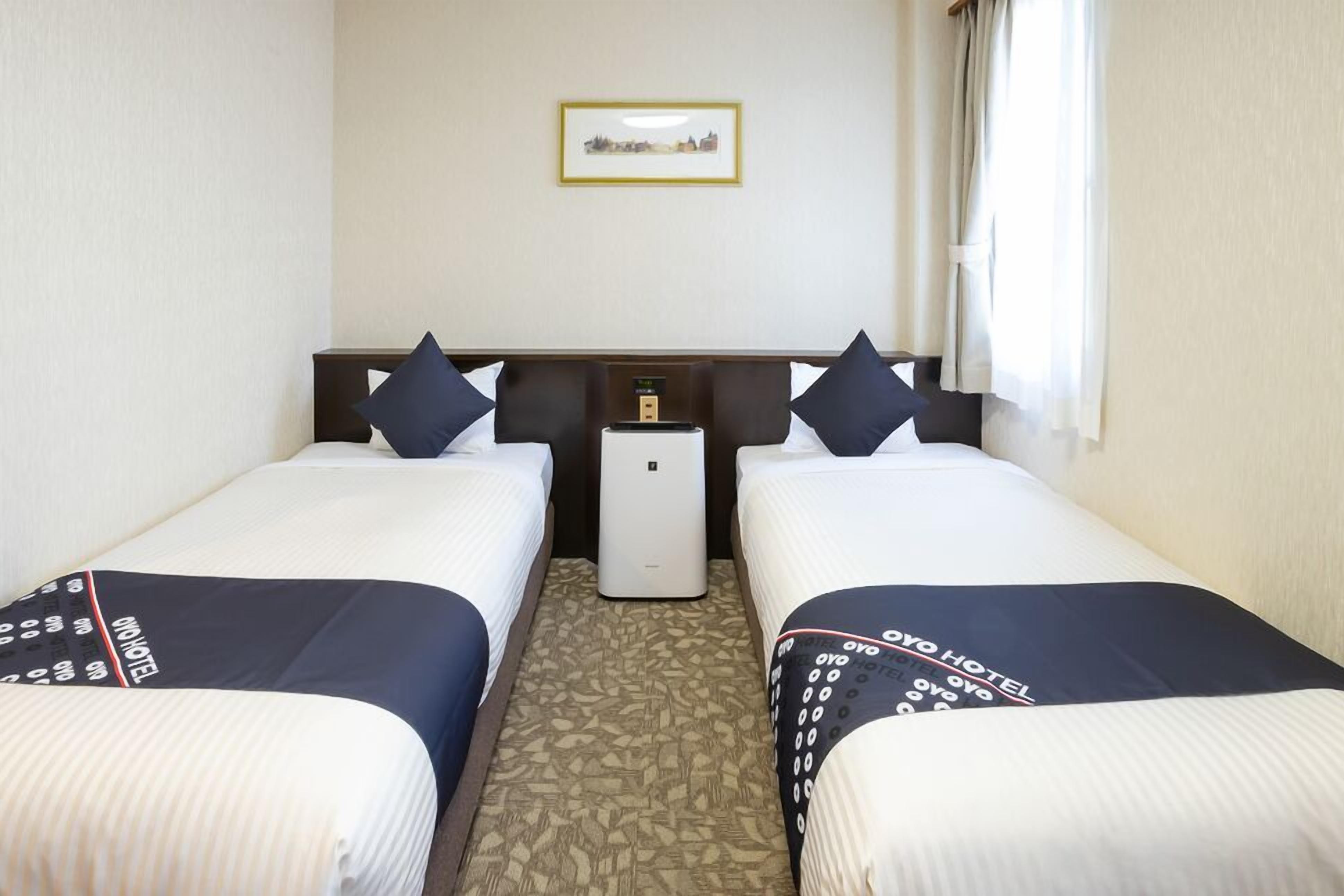 A hotel room with two beds, a nightstand, a small air conditioning unit, and a framed picture on the wall.