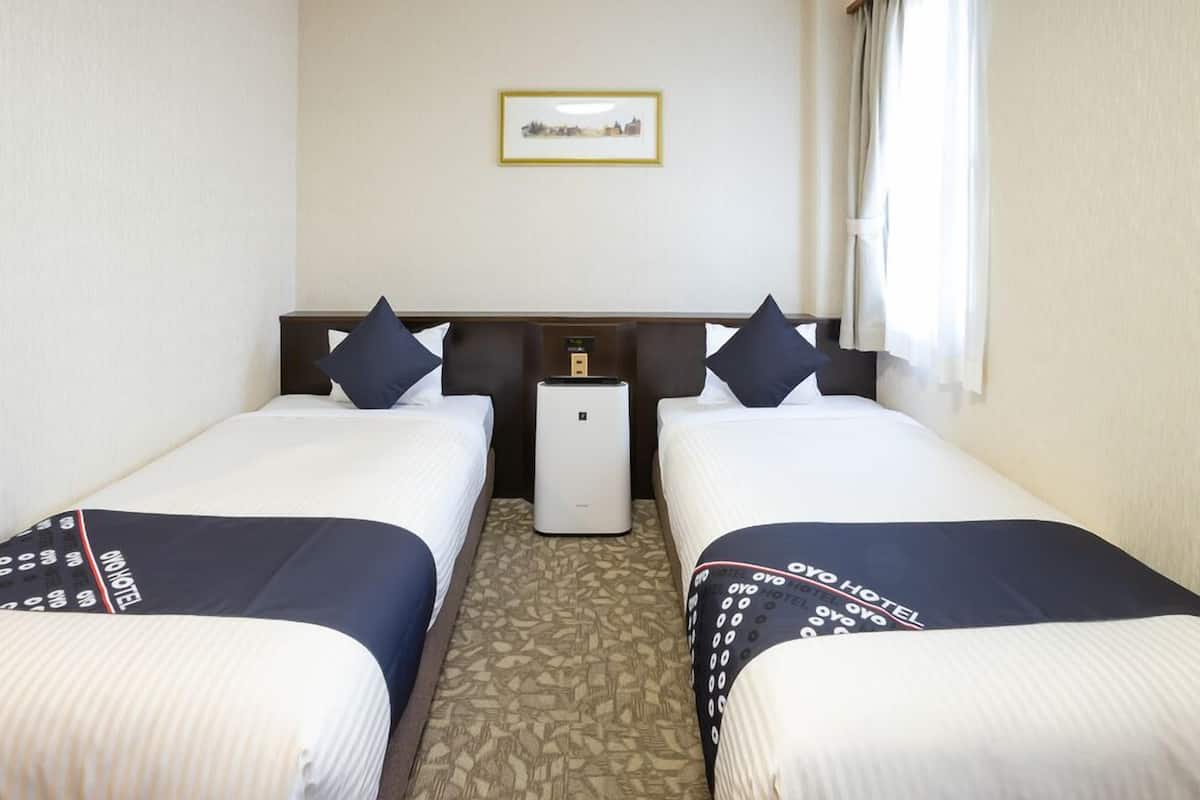 Ein Hotelzimmer mit zwei Betten, einem Nachttisch, einer Klimaanlage und einem gerahmten Bild an der Wand.