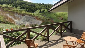 A balcony with wooden chairs and a table, overlooking a green valley and a cliff. - Manza Hotel Juraku (Tsumagoi)