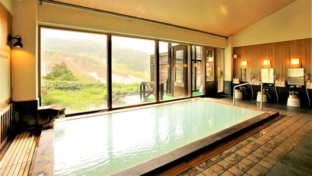 A large indoor swimming pool with a view of a mountainous landscape through large windows. - Manza Hotel Juraku (Tsumagoi)