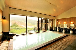A large indoor swimming pool with a view of a mountainous landscape through large windows. - Manza Hotel Juraku (Tsumagoi)