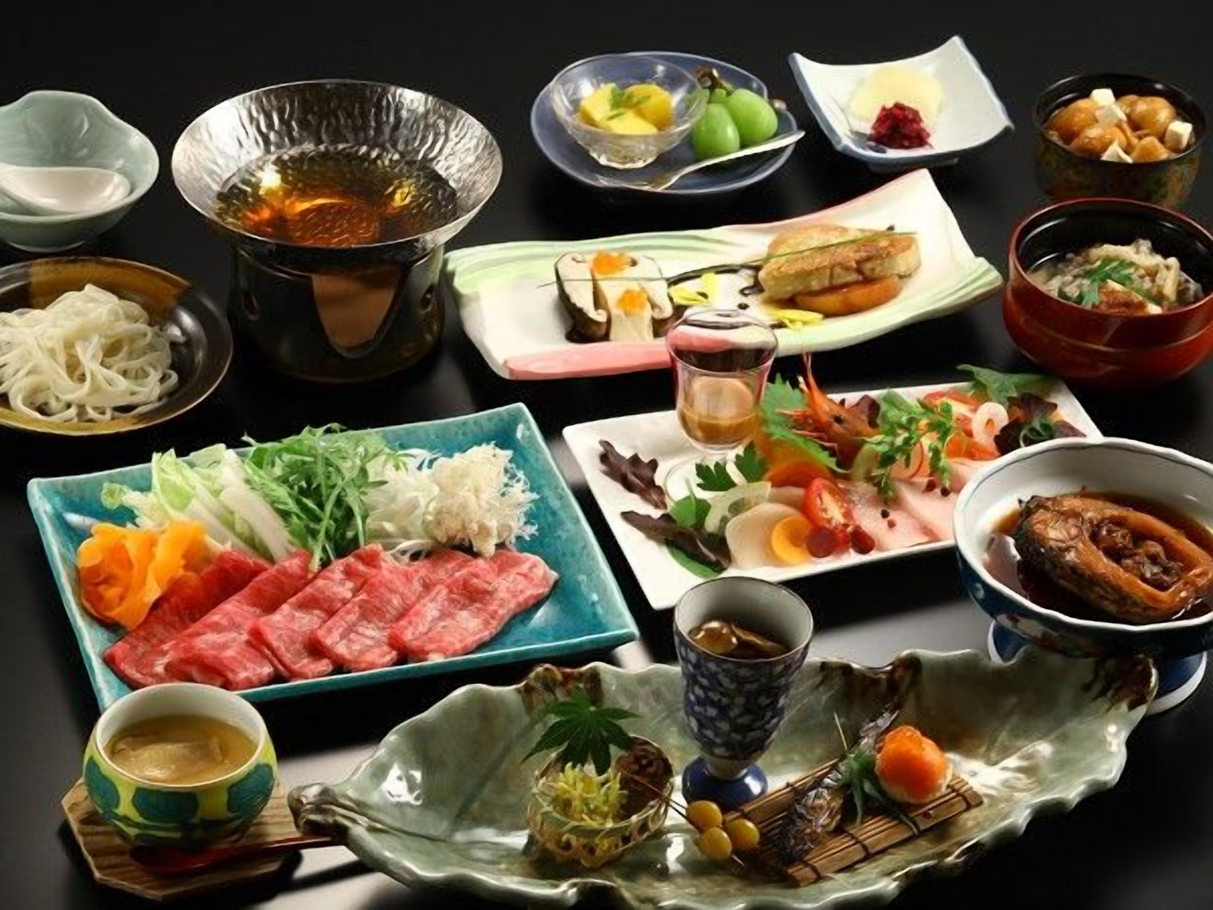 Una variedad de platos y bebidas sobre una mesa, incluyendo un recipiente con comida caliente, sashimi y un tazón de sopa.