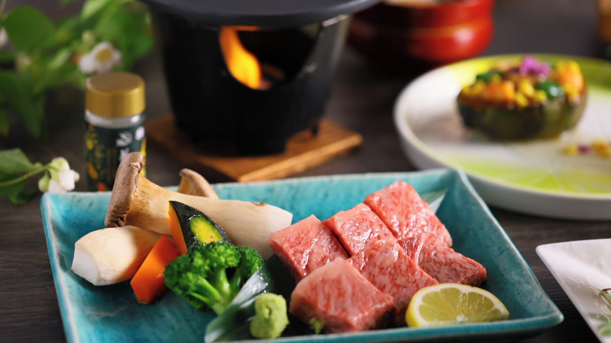 Una comida con diferentes verduras y carne, una olla con llama, y un plato con un guiso colorido.