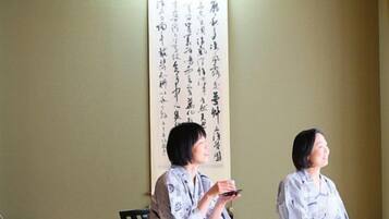 Dos personas sentadas sobre esteras de tatami en una habitación japonesa tradicional con un biombos shoji y un rollo de caligrafía en la pared.