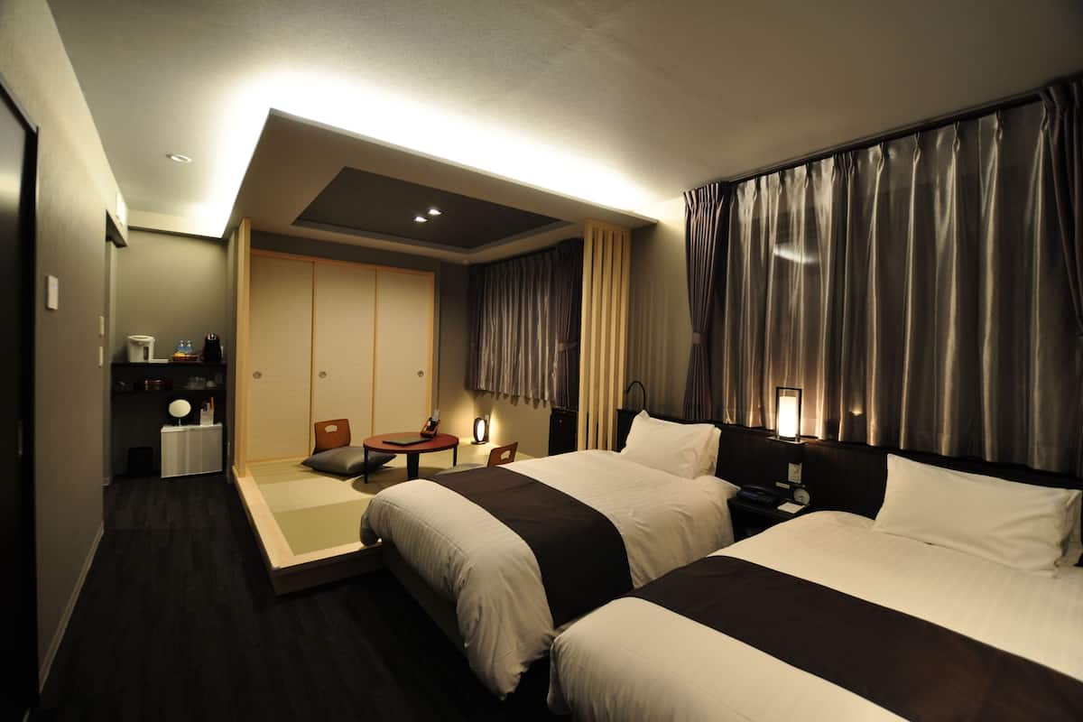 A hotel room with two beds, a desk, a chair, a small table, and a wardrobe.