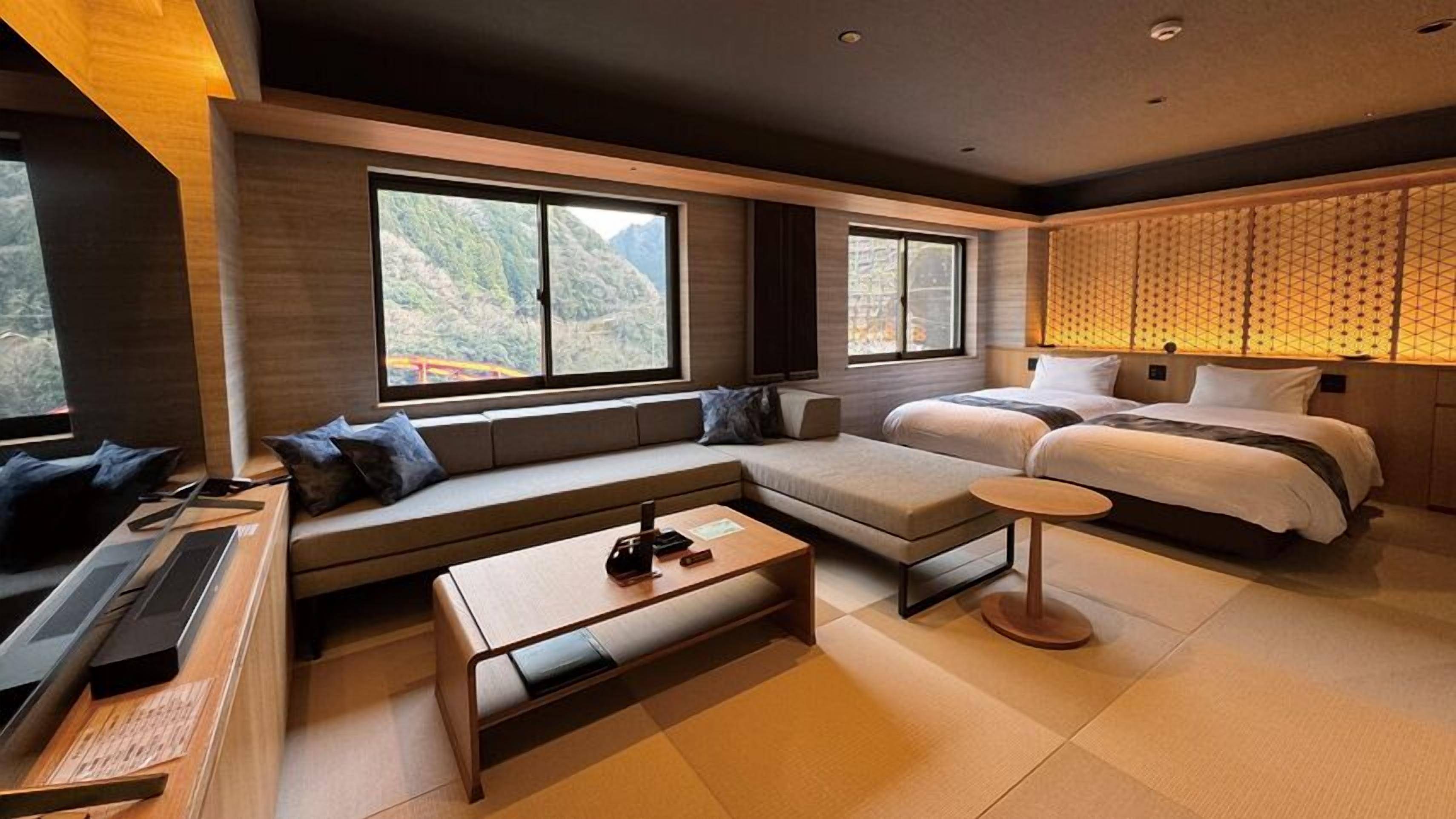 Habitación de hotel moderna con sofá, cama, una mesita y ventanas amplias con vistas a la montaña.