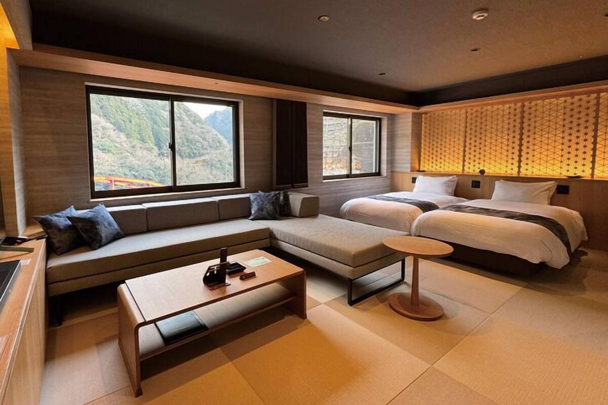 A modern hotel room with a sofa, a bed, a small table, and large windows offering a mountain view.