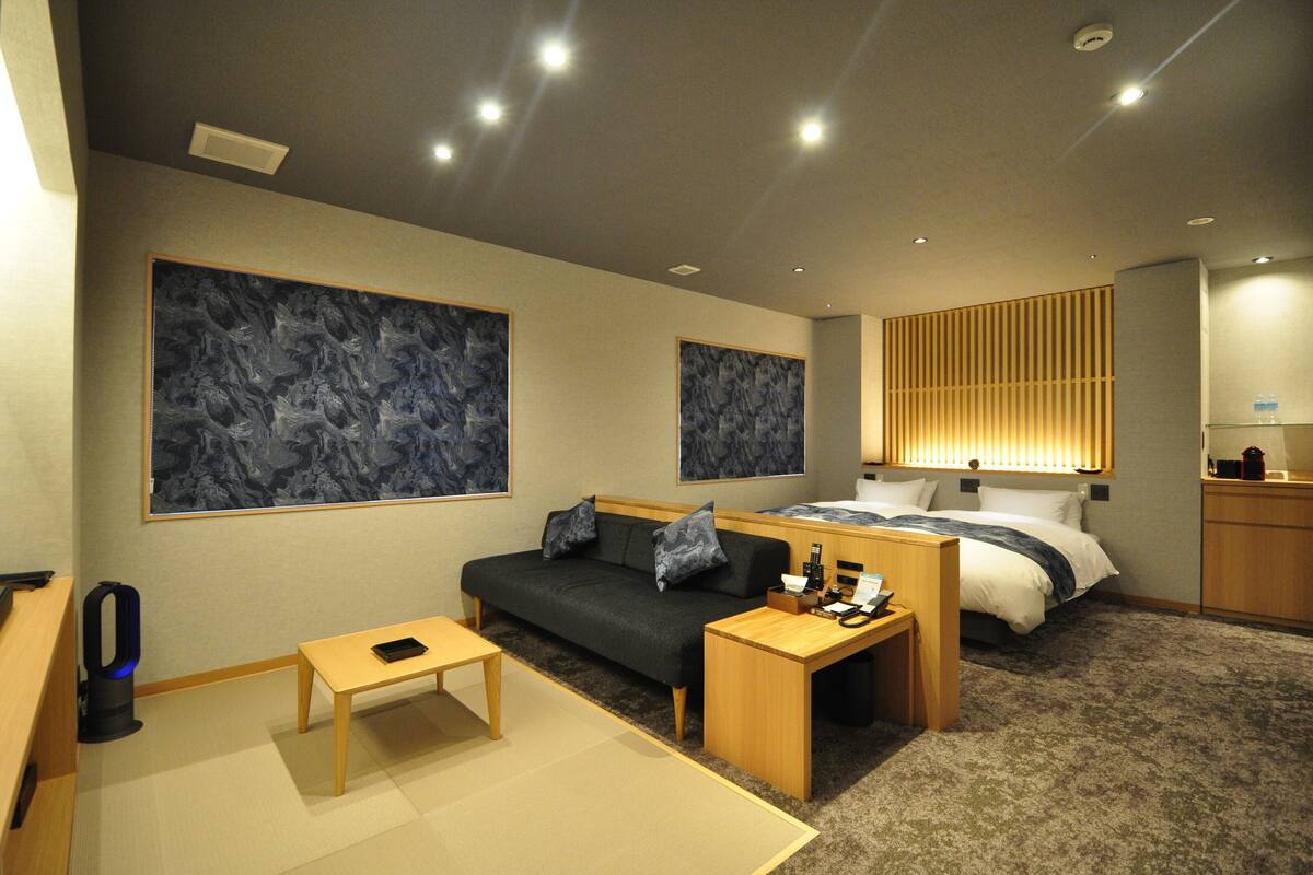 A modern hotel room with a sofa, a small table, a bed, and artwork on the walls.