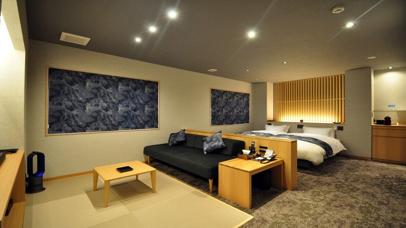 Una habitación de hotel moderna con sofá, cama, una mesita y obras de arte en las paredes.