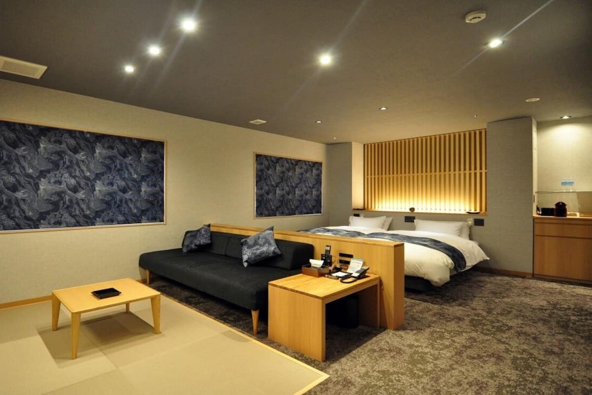 A modern hotel room with a sofa, a bed, a small table, and artwork on the walls.