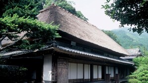 A traditional Japanese building with a thatched roof, wooden sliding doors, and a stone pathway leading to the entrance.