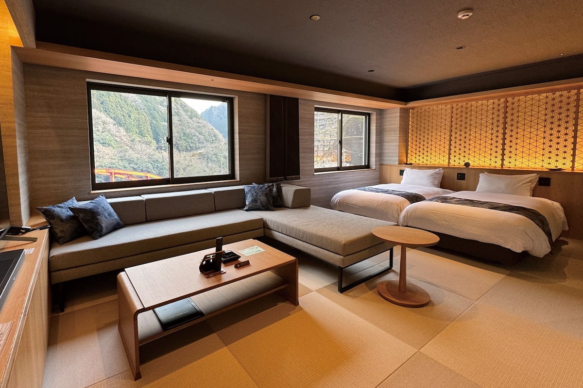 Una habitación de hotel moderna con sofá, cama, una mesita y grandes ventanales con vistas a la montaña.