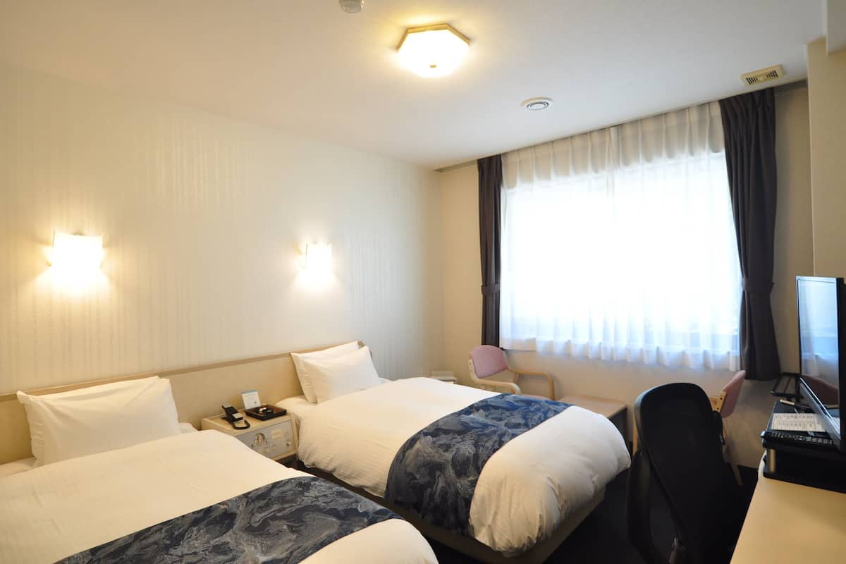 A hotel room with two beds, a desk with a computer, and a window with curtains.
