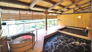 A wooden interior with a stone hot tub and a wooden tub with pink water.